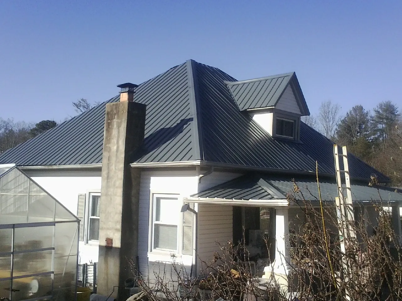 Dark blue standing seam metal roof on a white farmhouse with dormer — Slate & Tile Roof Repair by Roofing Brothers in West Alexandria