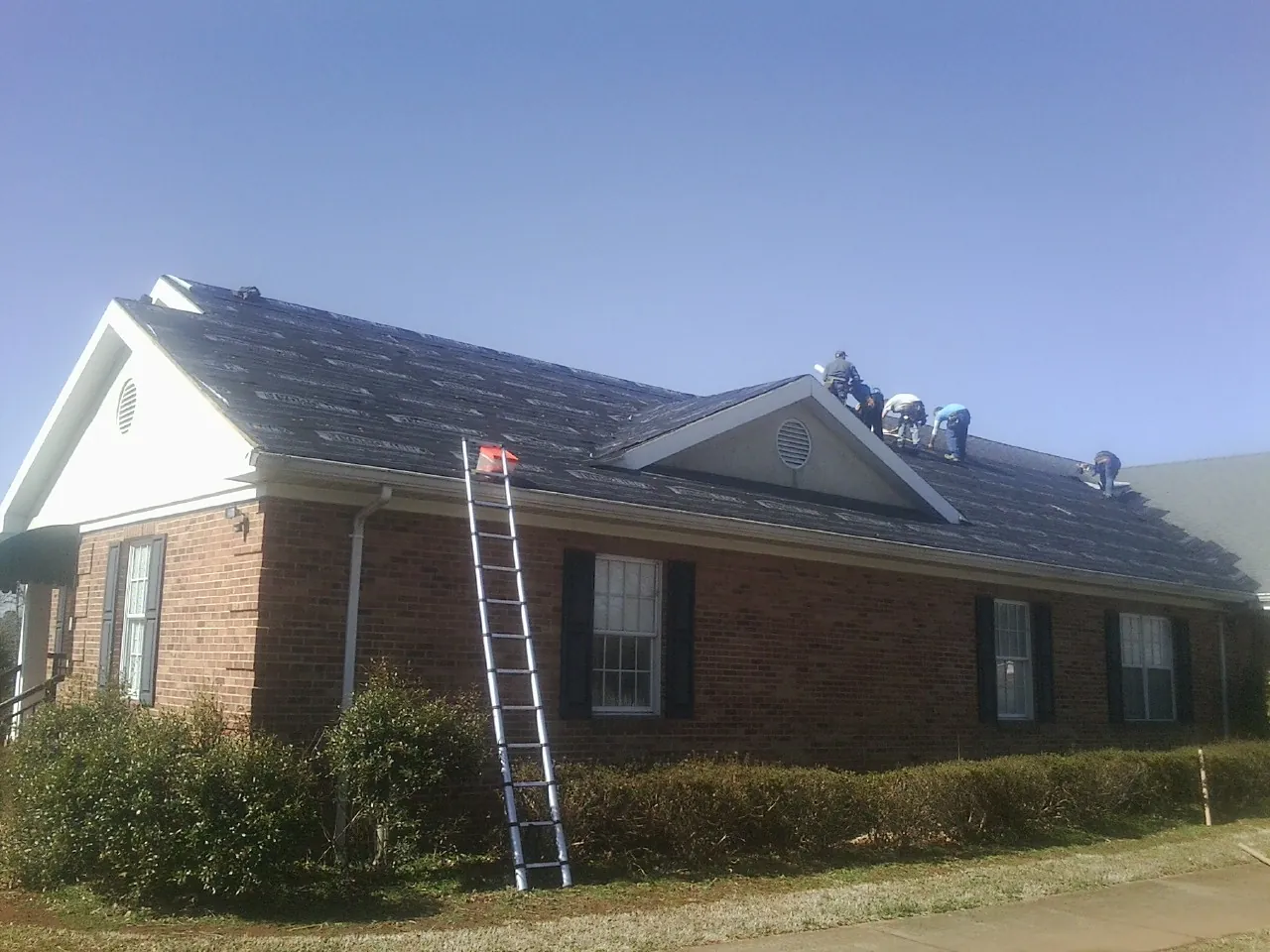 Crew tearing shingles off a brick ranch roof with a ladder set — Emergency Roof Repair work by our crew in West Alexandria