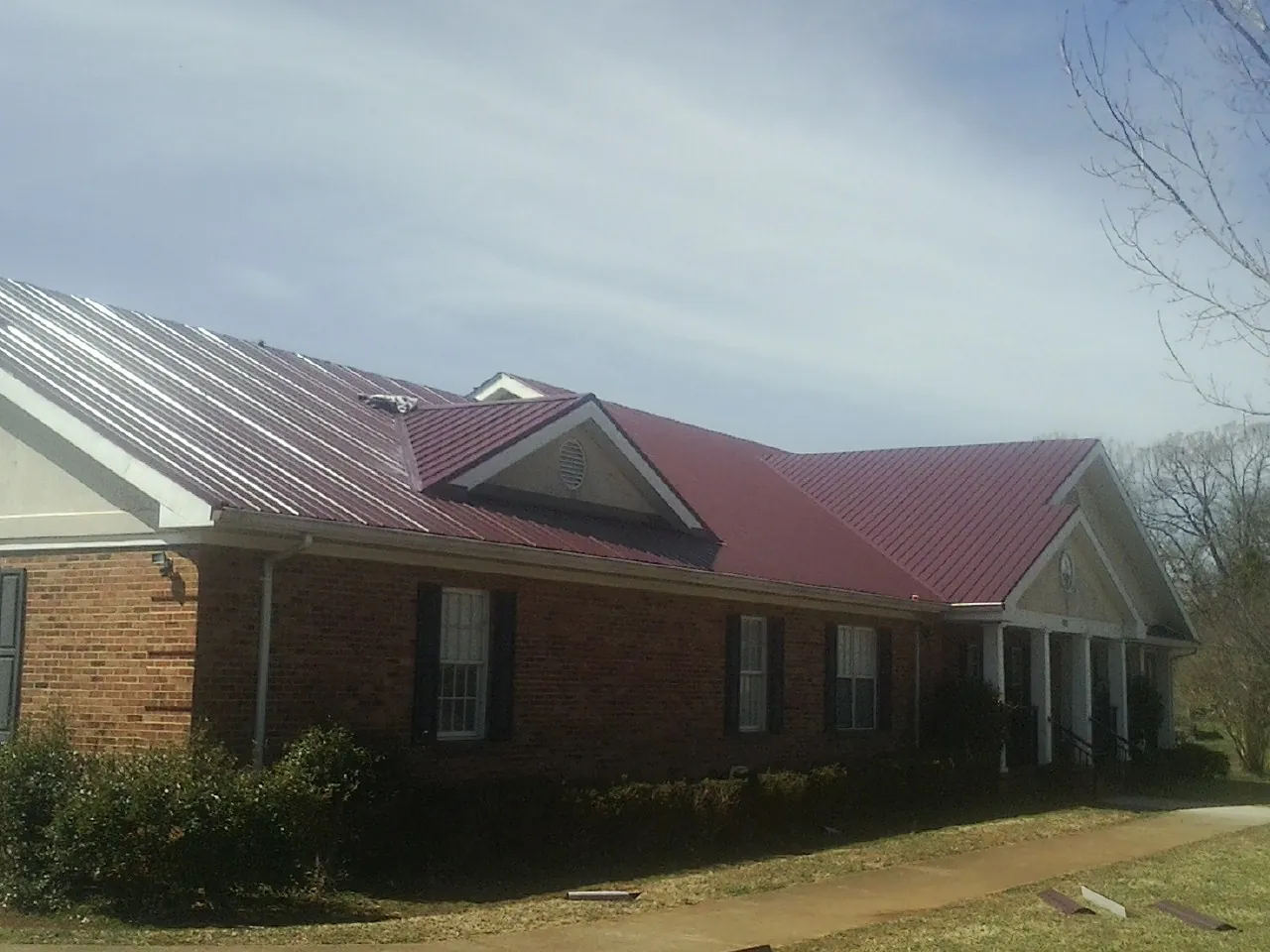 Red metal roof with gabled entries on a long brick building, from a Hail Damage Roof Repair job in West Alexandria