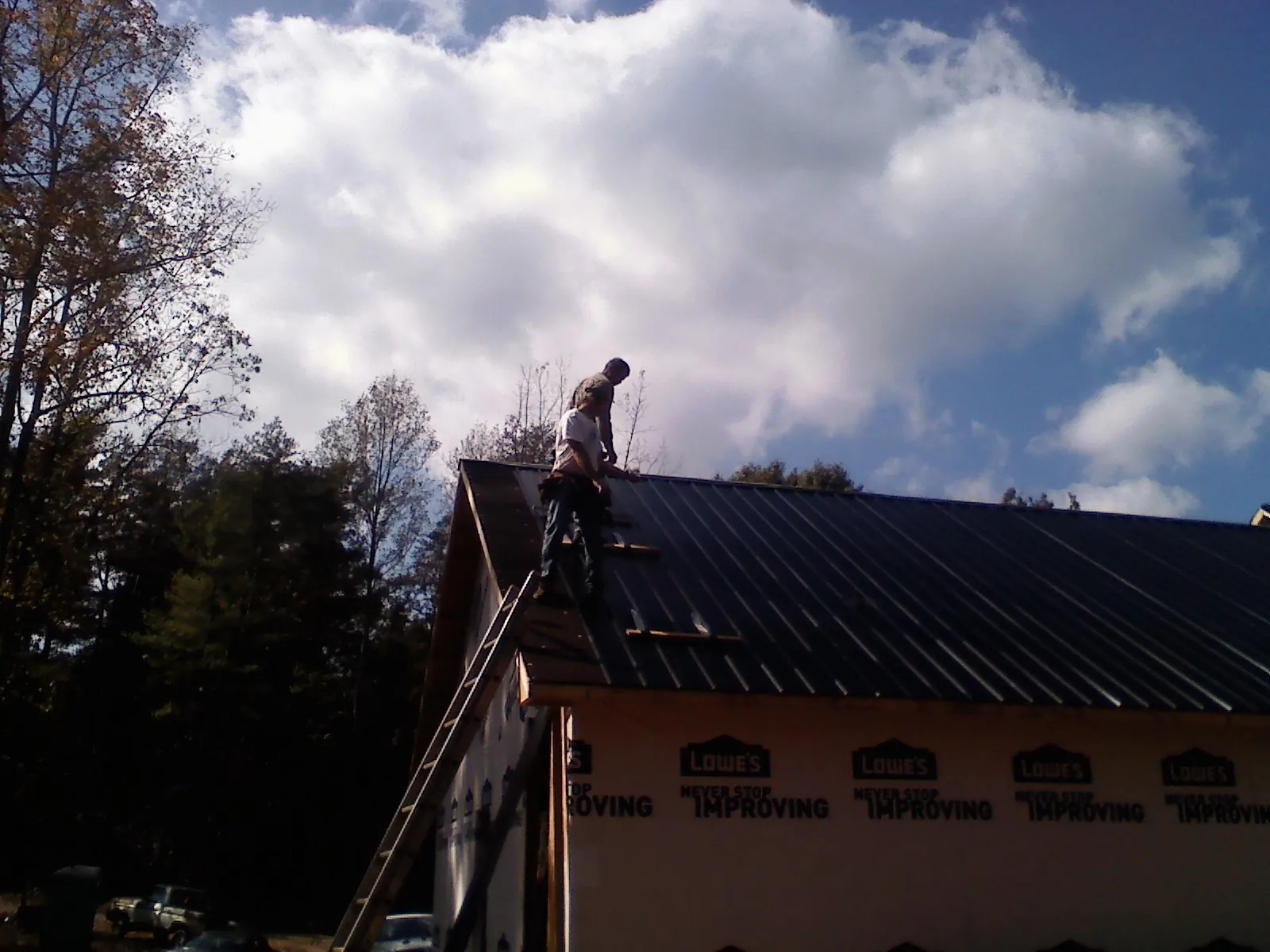 Roofer fastening dark metal panels high against a cloudy sky, from a Roof Inspection job in West Alexandria