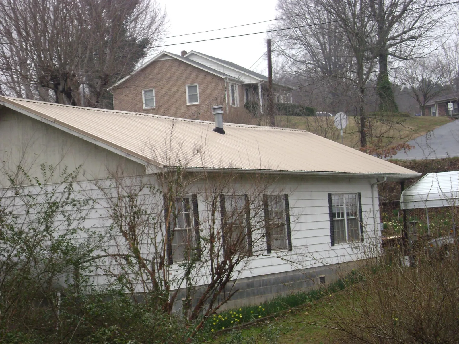 Tan metal roof on a white sided house set into a hillside — Commercial Roofing by Roofing Brothers in West Alexandria